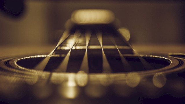 Close-up view of an acoustic guitar's strings and soundhole, captured with a shallow depth of field for a dramatic effect.