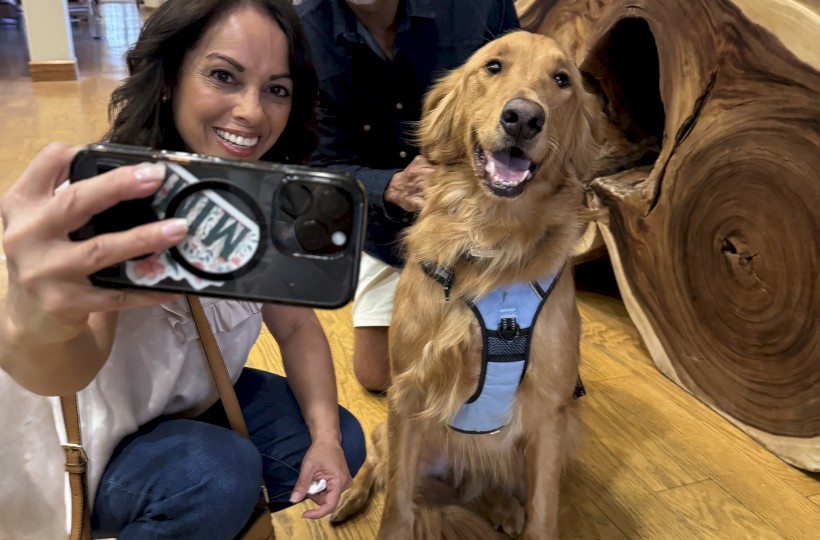 Two people and a golden retriever take a selfie in a warmly decorated indoor space.