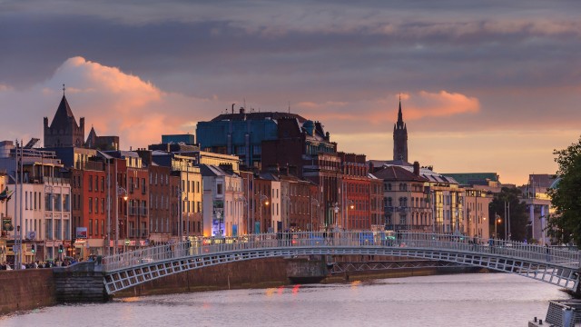 A picturesque view of a bridge over a river, flanked by historic buildings under a colorful sky at sunset or dusk.