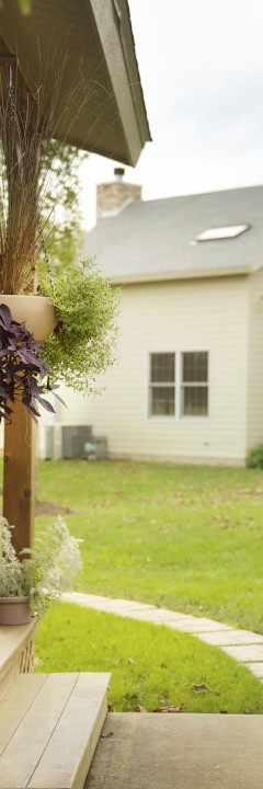 A yard with a pathway, plants, and part of a house leading to another house.