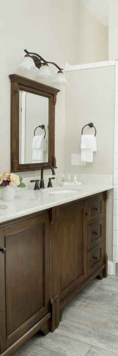 This image shows a bathroom with a double vanity, wooden cabinets, mirrors, light fixtures, and a glass-enclosed shower with tiled walls.