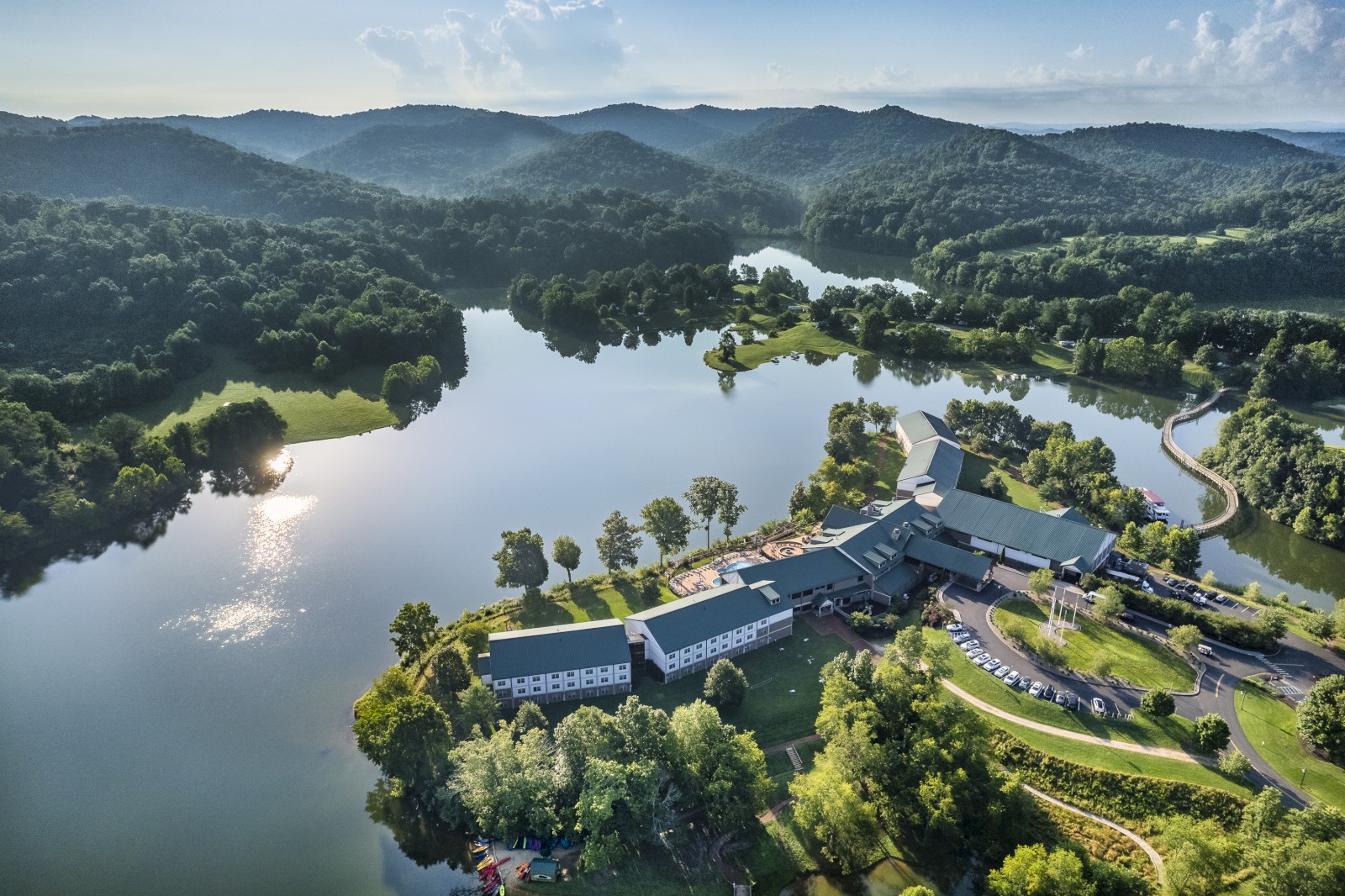 An aerial view of a large resort or estate surrounded by trees and lakes in a hilly area under a blue sky with scattered clouds.
