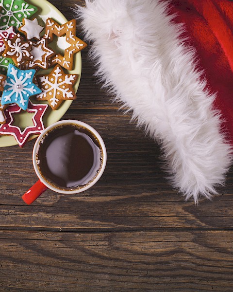 A plate of star-shaped cookies, a cup of hot chocolate, and a Santa hat on a wooden table surface.