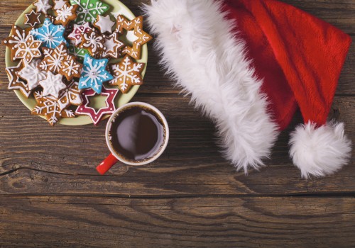 A plate of star-shaped cookies, a cup of hot chocolate, and a Santa hat on a wooden table surface.