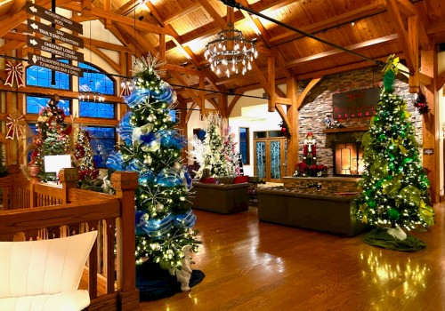 A cozy, festive indoor lounge with tall decorated Christmas trees, warm wooden beams, a stone fireplace, and comfortable seating in a lodge-style room.