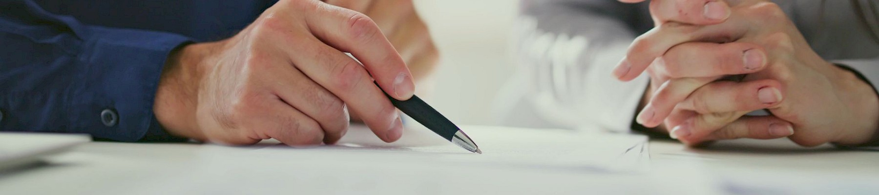 Two people signing a document or contract, hands and pen visible as they write.