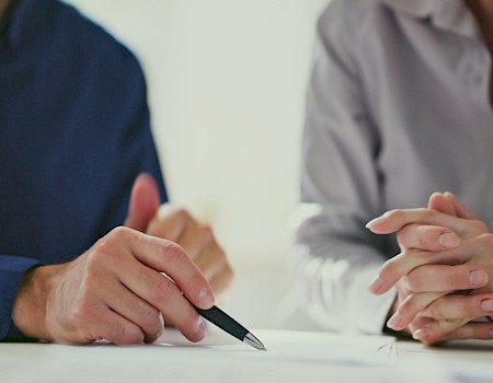 Two people signing a document or contract, hands and pen visible as they write.