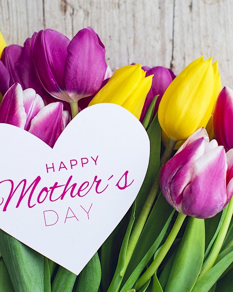 A bouquet of purple and yellow tulips with a heart-shaped card that says “Happy Mother’s Day.”