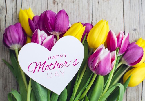 A bouquet of purple and yellow tulips with a heart-shaped card that says “Happy Mother’s Day.”