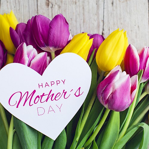 A bouquet of purple and yellow tulips with a heart-shaped card that says “Happy Mother’s Day.”