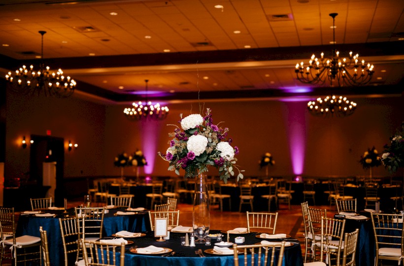 A banquet hall setup with round tables, elegant centerpieces, and warm lighting for a formal event, ending with a period.