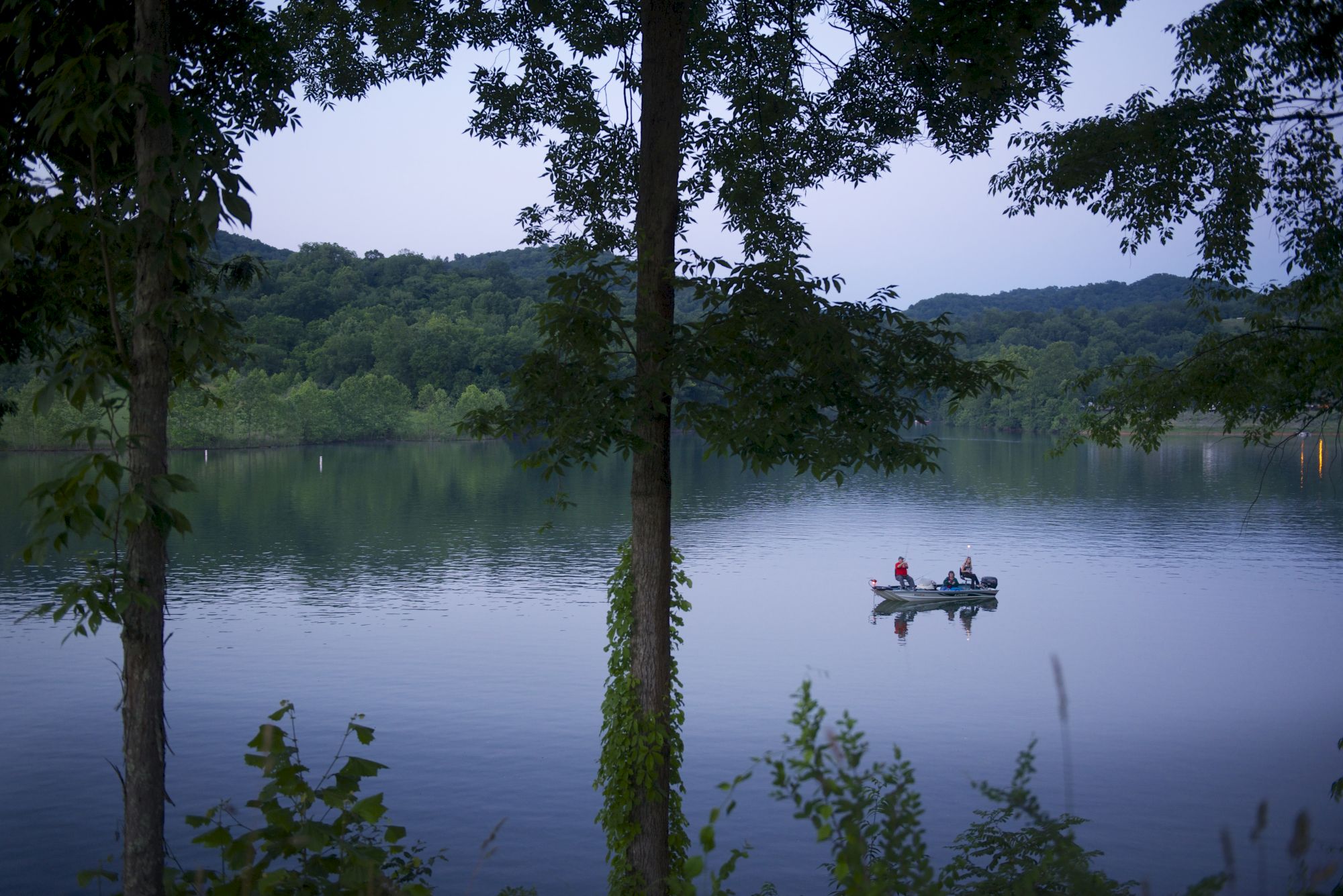 A serene lake scene with two people in a small boat, surrounded by trees and calm water, creating a peaceful and tranquil atmosphere.