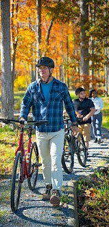 People enjoy a bike ride and walk together through a vibrant autumn forest on a sunny day.