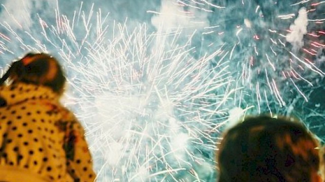 A crowd watches a fireworks display lighting up the night sky with bright bursts and trails, creating a festive, awe-filled atmosphere.