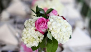 A floral centerpiece with pink roses and white hydrangeas on a pink and green table runner at a wedding reception.