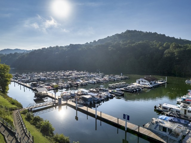 A scenic view of a marina with boats docked, surrounded by green hills and bright blue skies, captured during a sunny day.