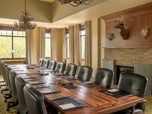 A cozy, elegant conference room with a long wooden table, black leather chairs, and hunting-themed decor including deer antlers and mounted heads.