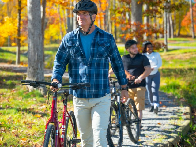 People enjoy a fall day biking and walking on a scenic trail surrounded by colorful autumn trees.