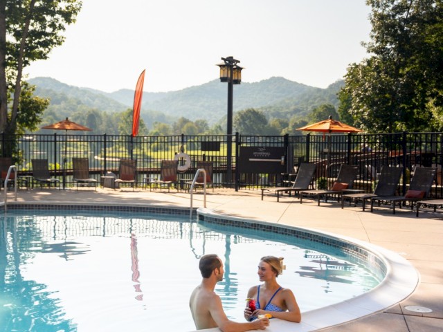 A couple enjoys a conversation in the pool at Mountain View Resort, surrounded by mountains, lounge chairs, and sunny weather.