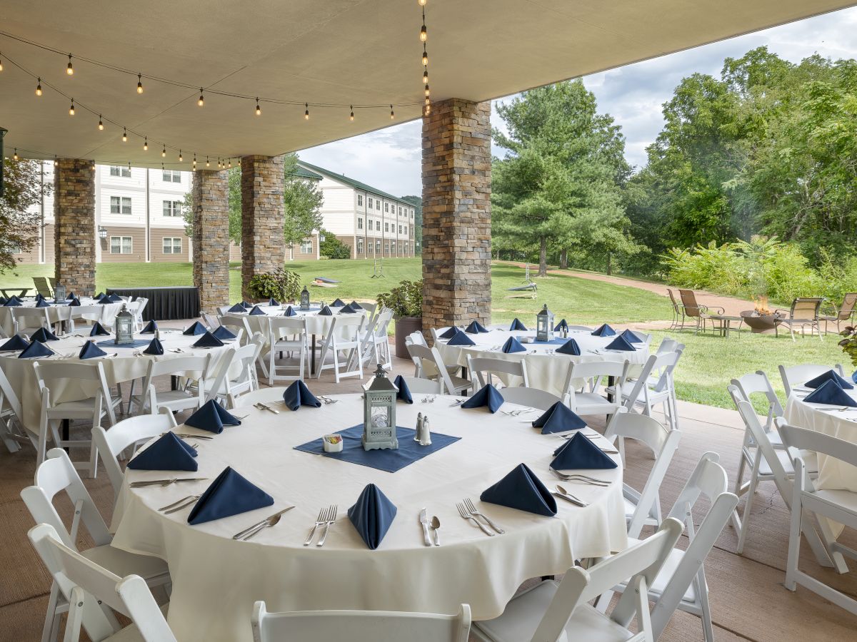 The image shows an outdoor event setup with round tables covered in white tablecloths, blue napkins, and white chairs, under string lights, ending the sentence.