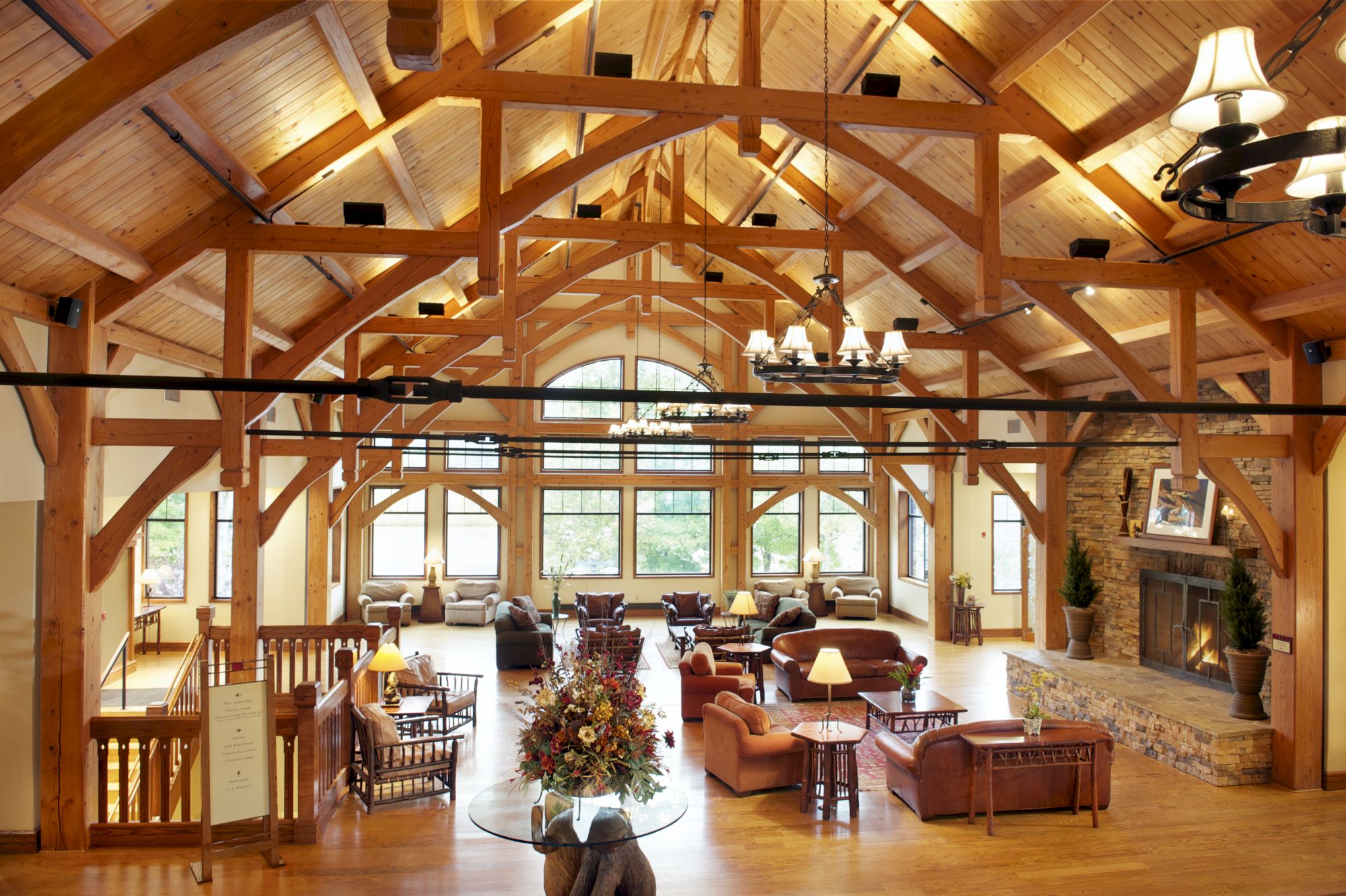 This image shows a spacious, wooden-beamed lodge interior with multiple seating areas, a grand fireplace, large windows, and a chandelier.