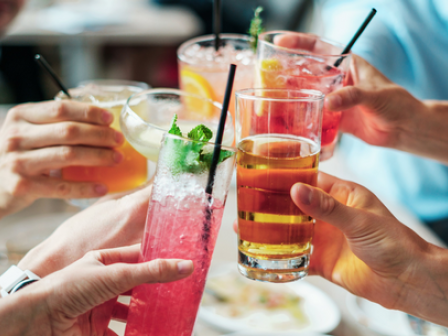 Several people are clinking glasses containing a variety of colorful beverages at what seems to be a celebratory gathering.