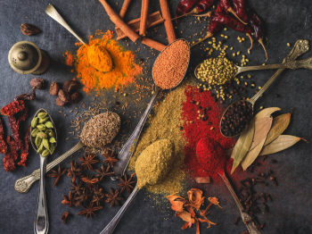 An assortment of spices, including cinnamon, turmeric, red chili, lentils, black pepper, star anise, cardamom, and bay leaves on a dark background.