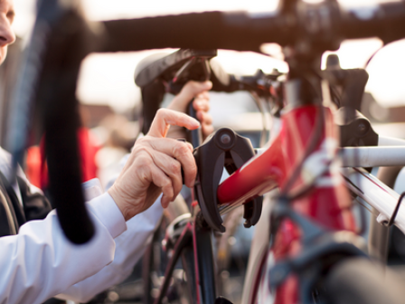 A person adjusts a red bicycle on a bike rack, wearing a white and black jacket, with a focus on the hand and bike components.