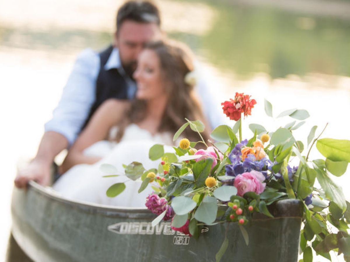A couple is sitting in a canoe adorned with flowers, enjoying a romantic moment on the water.