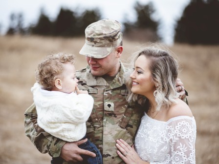 A soldier in uniform with a wife and child in a natural outdoor setting.