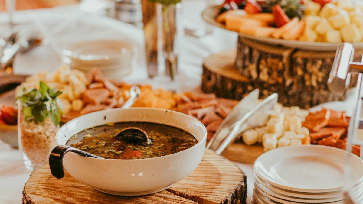 A beautifully arranged buffet with soup, fruits, cheese, and platters, decorated with wooden accents and elegant tableware.