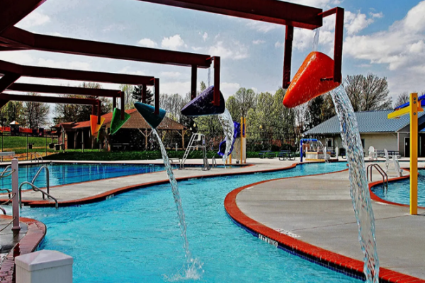 This image shows a water park play area with colorful tipping water buckets, a lazy river pool, and surrounding greenery ending the sentence.