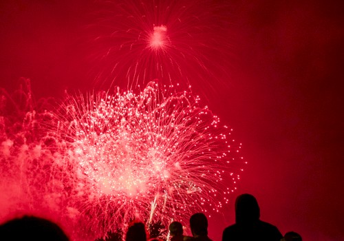 People watch a vibrant red fireworks display lighting up the night sky.