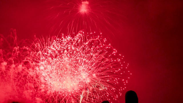People watch a vibrant red fireworks display lighting up the night sky.