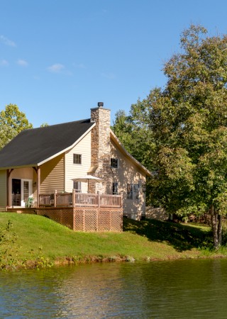 A house by the water with a deck, surrounded by trees and a clear blue sky on a sunny day.