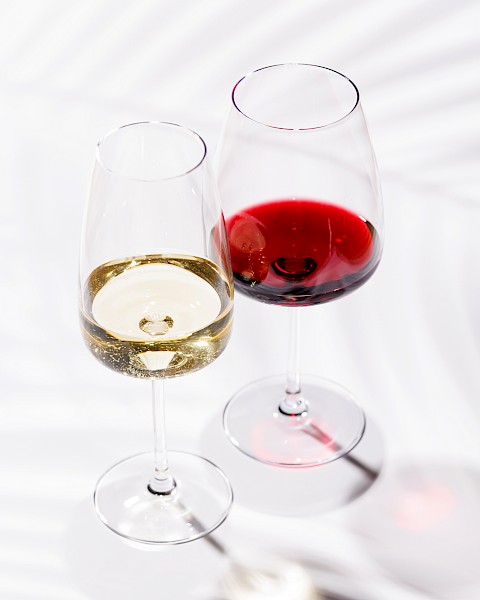 Two wine glasses, one with white wine and the other with red wine, on a white surface with shadows.