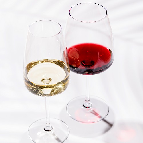 Two wine glasses, one with white wine and the other with red wine, on a white surface with shadows.