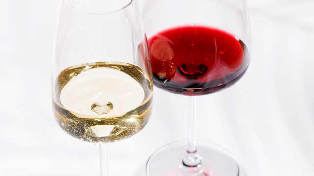 Two wine glasses, one with white wine and the other with red wine, on a white surface with shadows.