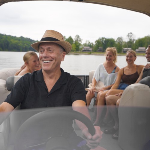 A group of five smiling people enjoys a boat ride on a lake on a cloudy day.