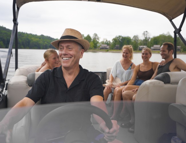 A group of five smiling people enjoys a boat ride on a lake on a cloudy day.