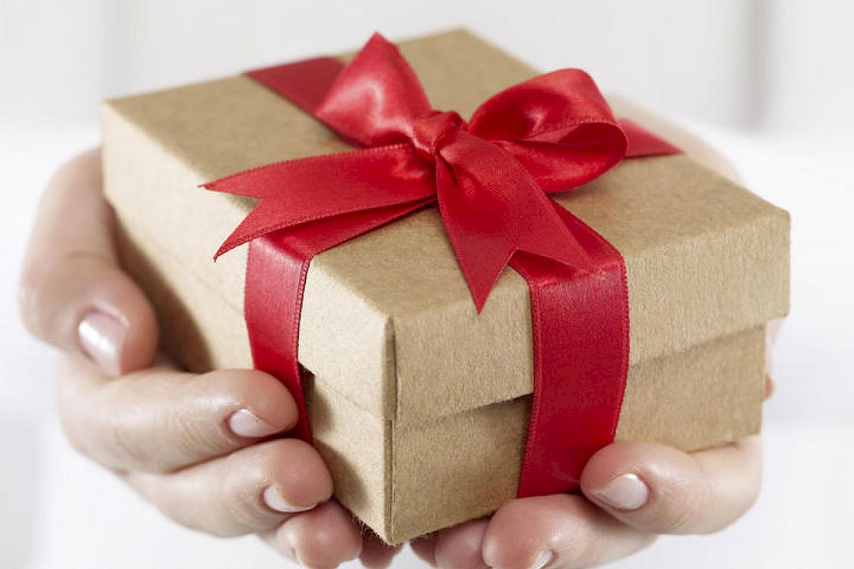 Hands are holding a small gift box wrapped in brown paper with a red ribbon bow, ready for presentation or gifting.