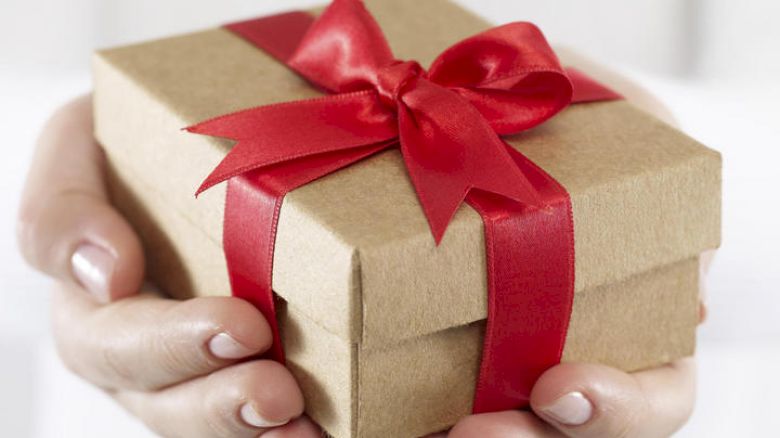 Hands are holding a small gift box wrapped in brown paper with a red ribbon bow, ready for presentation or gifting.