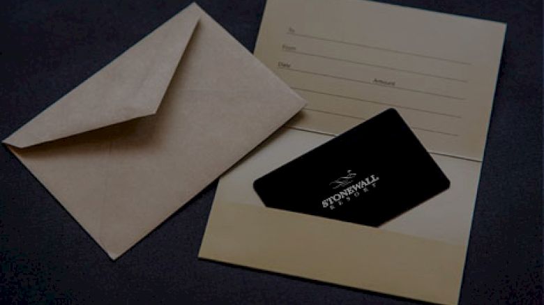 The image shows an open envelope next to a cardholder containing a black card. The cardholder has fields for name, date, and amount.