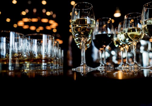 Several glasses of white wine and other beverages are arranged on a dark table with warm bokeh lights in the background.