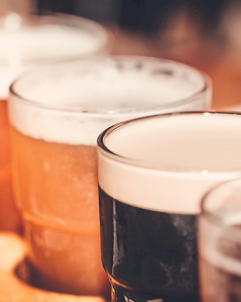 Several pints of beer are lined up on a wooden surface, with some beers darker and some lighter in color.