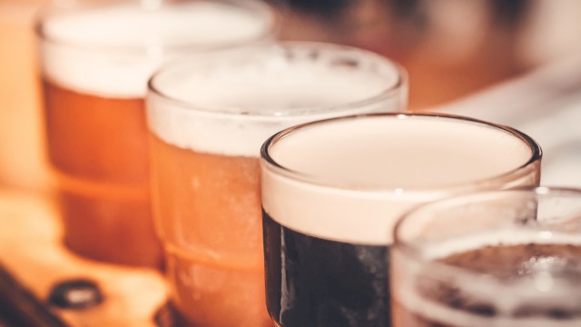 Several pints of beer are lined up on a wooden surface, with some beers darker and some lighter in color.