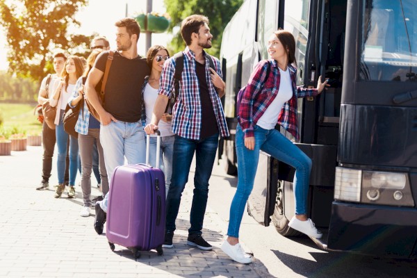 A group of young people are boarding a bus with baggage on a sunny day.