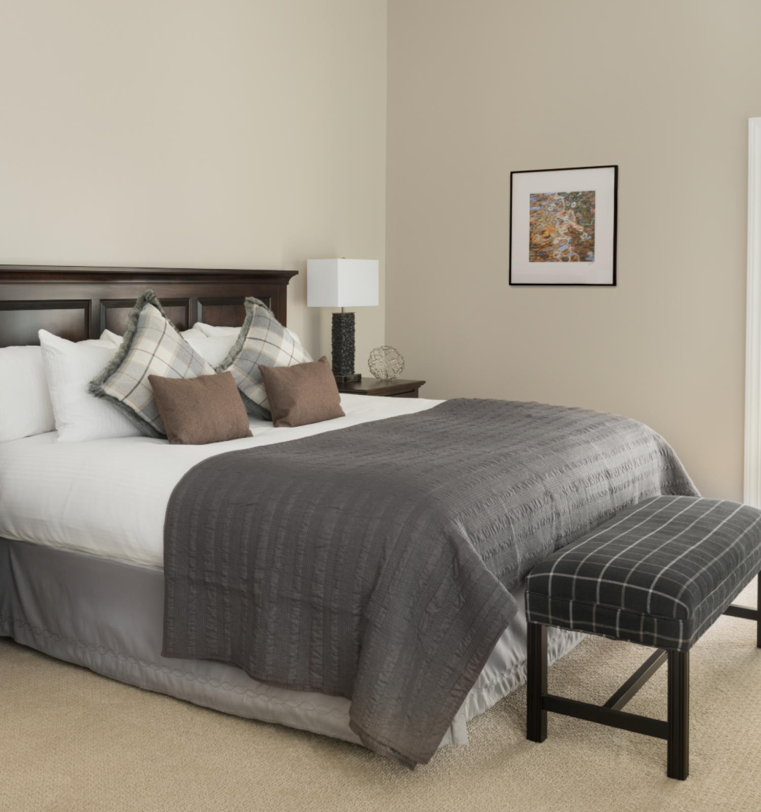 A neatly arranged bedroom with a large bed, nightstands, lamps, a bench at the foot, and an open door leading to a balcony with seating.