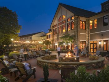 A cozy evening at a lodge with a fire pit, outdoor seating, string lights, and people enjoying the ambiance in front of a large building.