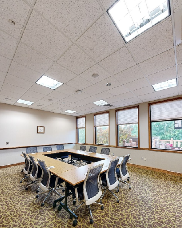 A spacious conference room with a U-shaped table, office chairs, large windows, and a wall clock in a professional setting.